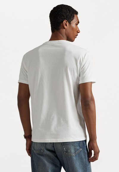 Tricou alb din bumbac, cu mâneci scurte, guler rotund și design simplu. Purtați cu blugi denim albaștri, evidențiind o croială casual.