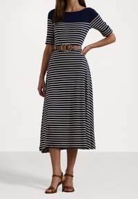 Pruhované midi šaty v námořnické modři a krémové barvě, s přiléhavým vrškem a rozšířenou sukní, stažené v pase hnědým opaskem s kulatou sponou.