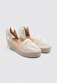 Espadrilles blancas trenzadas con una suela de yute, que cuentan con un talón abierto y lazos de cinta de satén. Tejido texturizado con un diseño de punta afilada.