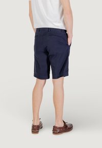 Pantaloni corti blu navy in twill di cotone, con tasche laterali e finitura orlata. Il modello indossa scarpe da barca marroni.