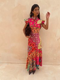 Multicolore, patchwork maxi-jurk met ruches aan de mouwen, bloemenpatronen en een uitlopende zoom. Draagt een bruine clutch en puntige hakken.