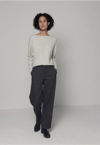 Hellgrauer, weicher Pullover mit langen Ärmeln, kombiniert mit dunkelgrauen, weit geschnittenen Hosen und schwarzen Schuhen, vor einem neutralen Hintergrund.