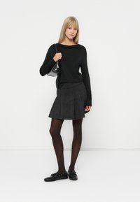 Haut noir à manches longues, jupe plissée grise, collants noirs et chaussures noires. Les accessoires comprennent un petit sac à main noir. Design simple et minimaliste.