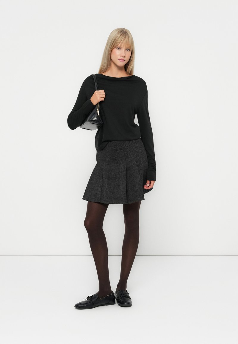 Haut noir à manches longues, jupe plissée grise, collants noirs et chaussures noires. Les accessoires comprennent un petit sac à main noir. Design simple et minimaliste.