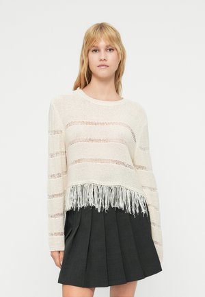 Lett, kremfarget strikkegenser med åpen vev og horisontale striper, avsluttet med frynsekant. Lange ermer og avslappet passform.