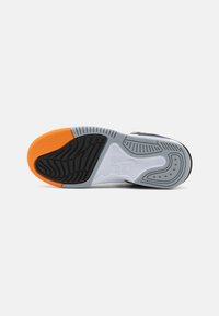 Suela de zapatilla con goma negra, entresuela gris y acento naranja. Presenta patrones texturizados y surcos para tracción.