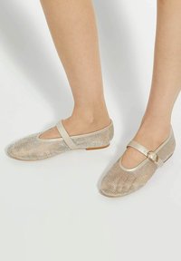 Glittering gold ballet flats with a rounded toe and ankle strap, featuring a textured mesh upper and a low, flat sole.