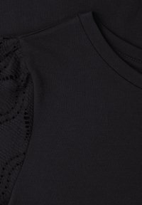 Černá látka zblízka ukazující kulatý výstřih a strukturovaný krajkový rukáv s vlnitými okraji.