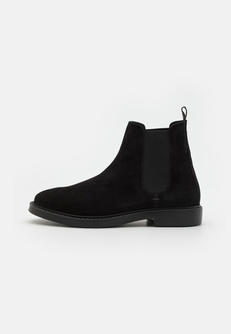 Bottes chelsea en suède noir avec des panneaux latéraux élastiques, bout rond, semelle plate et languette à l'arrière pour un enfilage facile.