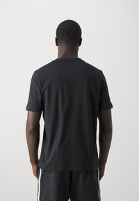 Czarny bawełniany t-shirt z krótkim rękawem i klasycznym okrągłym dekoltem, charakteryzujący się gładką teksturą i luźnym krojem, widziany od tyłu.