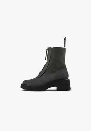 Šedá semišová kotníková bota s masivní černou gumovou podrážkou, bočním zipem a smyčkou na zadní straně; hladká textura a minimalistický design.