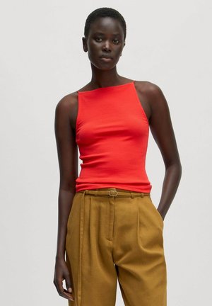 Rotes geripptes Tanktop mit quadratischem Ausschnitt und dünnen Trägern, kombiniert mit hochgeschnittenen braunen Hosen, die über einen Gürtel und Seitentaschen verfügen.