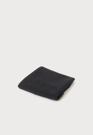 Serviette en tissu éponge noire pliée sur un fond clair uni, montrant une texture douce et des bords soigneusement finis.