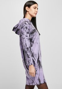 Fialová tie-dye mikinová šaty s dlhými rukávmi, bočnými rozparsekami, vyrobené z mäkkej látky, s voľným strihom a kapucňou. Čierne akcenty po celom oblečení.