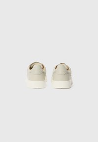 Zapatillas gris claro con una textura suave, suela de goma blanca y detalles de costura sutiles en el talón. Vista trasera con diseño de perfil bajo.