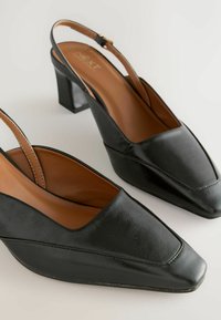 Čierne kožené slingback podpätky so štvorcovým špičkou, stredne vysokým blokovým podpätkom a hnedou vnútornou podšívkou. Obsahujú jemné švy.