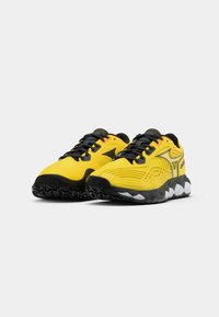 Baskets de sport jaunes avec des lacets et des accents noirs. Tige texturée avec des motifs ondulés. Semelle épaisse noire avec des éléments blancs à la base.