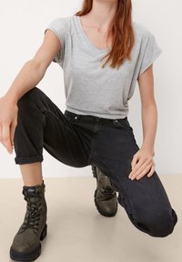 Szara koszulka z dekoltem w serek, czarne podwinięte jeansy oraz zielone botki za kostkę z grubą podeszwą i sznurowaniem. Gładka tkanina, casualowy krój i solidna konstrukcja.