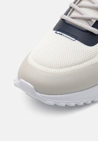 Könnyű sneaker, l�élegző fehér hálós felsőrésszel, szürke kiegészítőkkel és texturált bézs orrrésszel, fehér gumitalppal.
