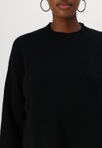 Pull noir côtelé avec un col rond et des épaules tombantes, doté d'un tissu texturé et d'un détail de col légèrement effiloché.