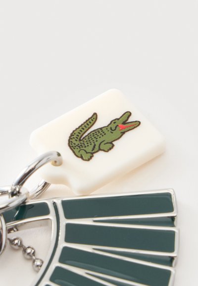 Porte-clés avec une étiquette rectangulaire blanche comportant une illustration de crocodile vert et des segments d’émail vert foncé attachés à un anneau en métal.