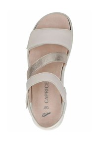 Lys rosa sandal med metalliske stroppedetaljer, lavet af glat materiale. Har et åbent tådesign og polstret indersål. Mærket "Caprice" synligt.