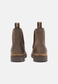 Braune Leder-Ankle-Boots mit elastischen Seitenpaneelen, strukturierten braunen Sohlen und markierten Zuglaschen an der Rückseite. Genähte Details an den Seiten.