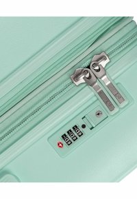 Valigia rigida verde menta con doppie cerniere argentate e lucchetto a combinazione con simbolo di sicurezza per i viaggi in rosso. Dettaglio della superficie testurizzata.