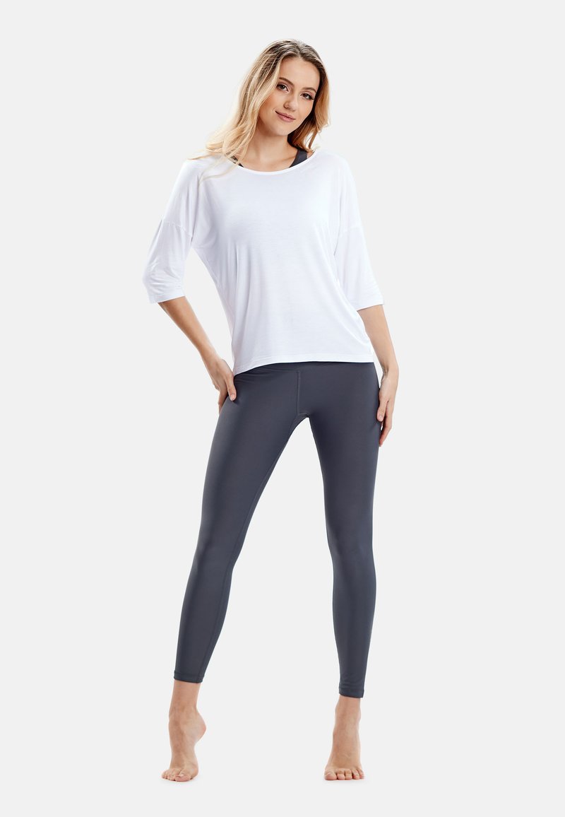 Witte losvallende top met driekwartmouwen, gecombineerd met strakke donkergrijze leggings. Zacht, glad stof zonder zichtbare patronen.