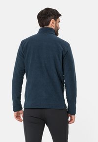 Fleece jacket in dark blue, with a high collar and long sleeves. Features a smooth texture and a slightly tailored fit. Adjustable cuffs.