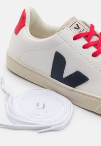 Białe skórzane sneakersy z granatowym logo, czerwonymi akcentami i białymi sznurowadłami. Zaokrąglony czubek i teksturowane detale przeszycia na cholewce.