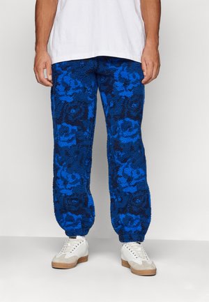 Blauwe fleecebroek met bloemenpatroon en een zachte, gestructureerde oppervlakte. Elastische tailleband en boorden; gecombineerd met witte sneakers.