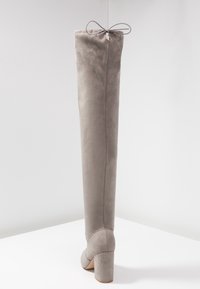 Bota de ante gris por encima de la rodilla con un gran eje, tacón cilíndrico y un detalle de lazada en la parte superior. Textura suave y acento de costura.