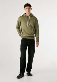 Olijfgroene hoodie met een voorzak en trekkoorden, gecombineerd met donkere jeans en zwarte schoenen, met een relaxte pasvorm en een katoenmix materiaal.