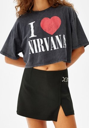 Kobieta nosząca krótką czarną koszulkę z napisem "I love Nirvana" oraz czarną mini spódniczkę z bocznym rozcięciem i srebrną klamrą.