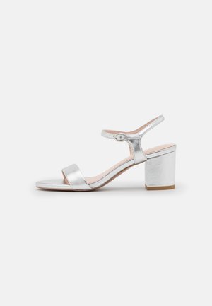 Sandal en métal argenté à talon haut avec une bride de cheville, une large bande à l'avant et un talon bloc, au texture lisse. Conçu pour le confort et le style.