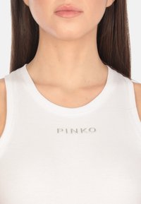 Top in tessuto a coste di colore bianco con scollatura rotonda. Logo "PINKO" in argento centrato sul petto. Texture liscia, design aderente.