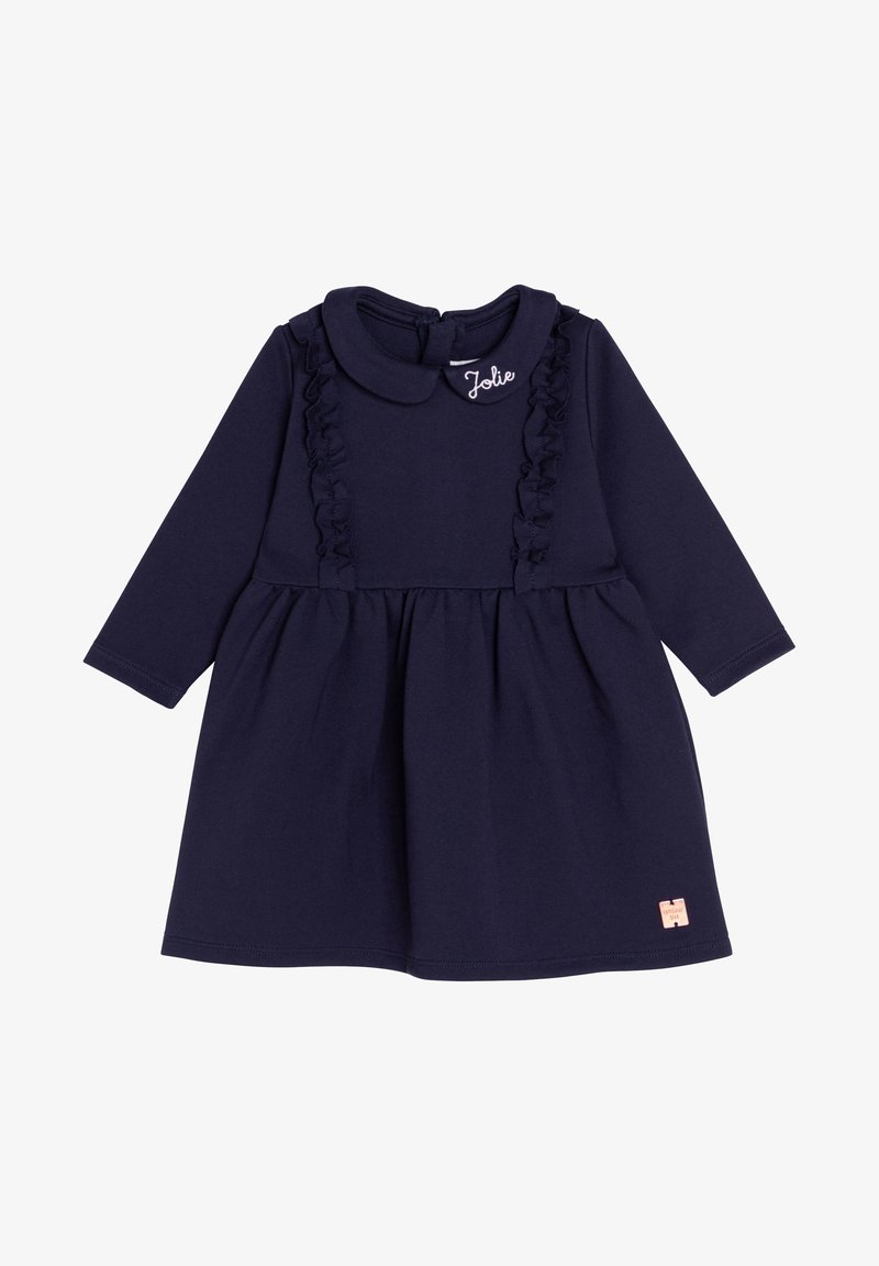 Robe bébé bleu marine à manches longues avec panneaux froncés, col rond brodé "Jolie" et petite étiquette beige près de l'ourlet.