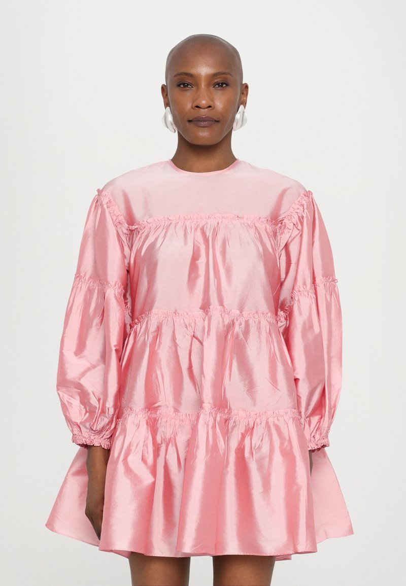 Ροζ σατέν φόρεμα με tiered σχέδιο, μακριά φουσκωτά μανίκια, πτυχώσεις στη μέση και στρογγυλή λαιμόκοψη. Λείος υφή με γυαλιστερή φινίρισμα.