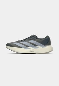 Zapatilla deportiva gris con tres franjas horizontales de color azul claro, parte superior lisa, puntera texturizada y una suela blanca gruesa con marca.