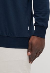 Marineblaue Sweatshirt mit gerippten Bündchen und unterem Saum. Leichtes Material mit glatter Textur. Seitenlabel in der Nähe des Saums sichtbar.