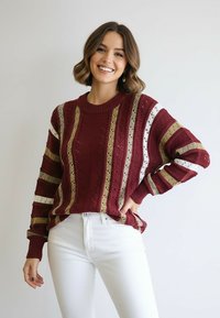 Bordowy sweter dziany z pionowymi paskami w kolorach złotym, białym i bordowym. Posiada okrągły dekolt i długie rękawy o luźnym kroju.