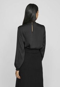 Svart blus med långa ärmar, slätt satängmaterial och figursydd silhuett. Har en nyckelhålstängning bak samt en ribbade svart kjol.