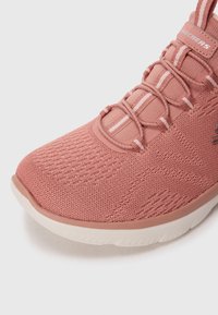 Pink athletic shoe with a textured mesh upper, rubber sole, and elastic lace system. Features a structured toe cap and subtle side accents.