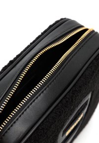 Borsa nera con texture in lana, dotata di rifiniture in pelle liscia e dettaglio della cerniera in oro. Cerniera parzialmente aperta che svela l'interno.