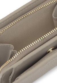 Interior de cartera de cuero beige que muestra cremallera dorada, compartimento forrado de tela y cierre de botón a presión con bordes cosidos.