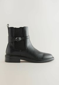Must musta ankle saapad elastsete külgpaneelidega, lame tallaga ja dekoratiivse pandlaga. Sile tekstuur ja ümar toe disain.