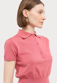 Rosa strikket polo-skjorte med klassisk krage, kort erm og fire knapper, med fasong som fremhever livet og en jevn tekstur.