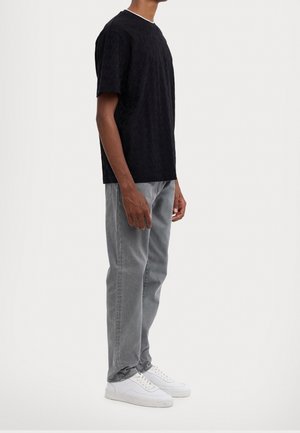 T-shirt noir à manches courtes avec motif texturé ; jeans gris ; baskets blanches ; design minimaliste avec un col rond et une coupe droite.