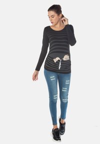 Schwarzes Langarmoberteil mit horizontalen Streifen, mit einem verspielten Grafikdesign eines Babys. Kombiniert mit ausgebleichten blauen Jeans und schwarzen Turnschuhen.